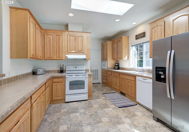 kitchen with white appliances, under cabinet range hood, a skylight, a sink, and light brown cabinetry