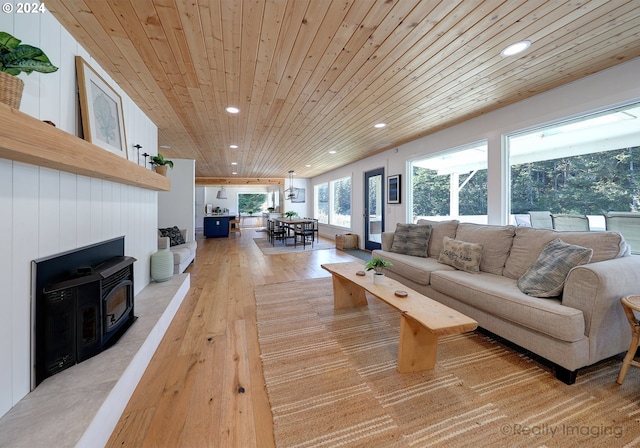 living room featuring light wood-type flooring, wood walls, a wood stove, and wooden ceiling