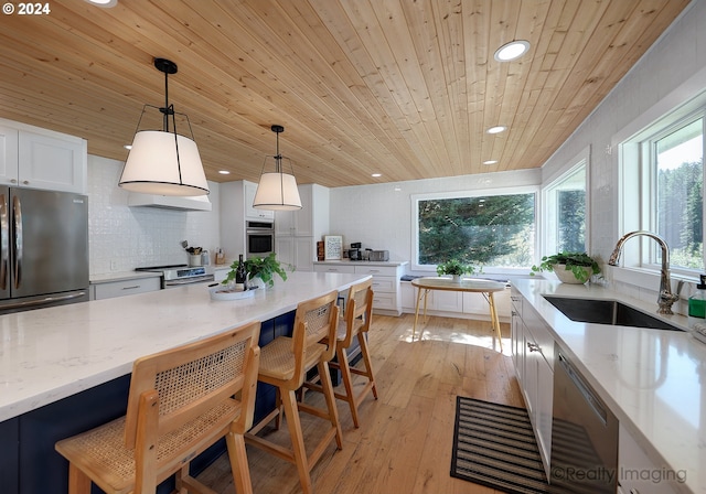 kitchen with pendant lighting, sink, light hardwood / wood-style flooring, appliances with stainless steel finishes, and light stone countertops