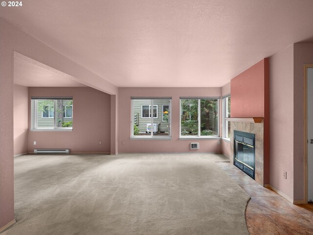 unfurnished living room featuring a wall mounted AC, a textured ceiling, a tiled fireplace, light colored carpet, and a baseboard radiator