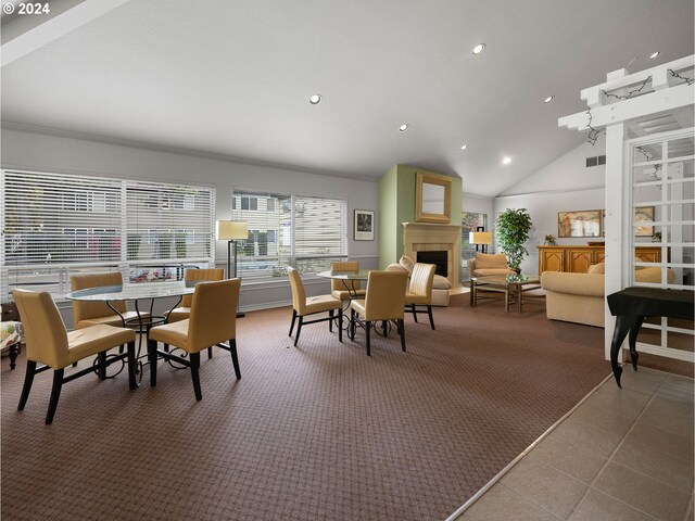 carpeted dining space with high vaulted ceiling and a tiled fireplace