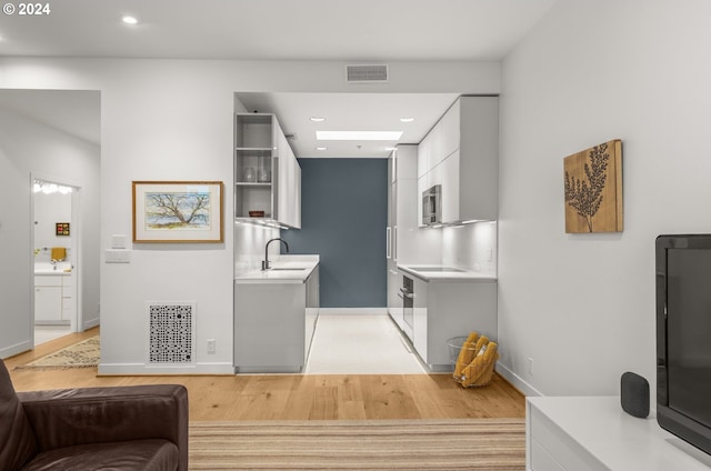 interior space featuring white cabinetry, light wood-type flooring, black electric stovetop, and sink