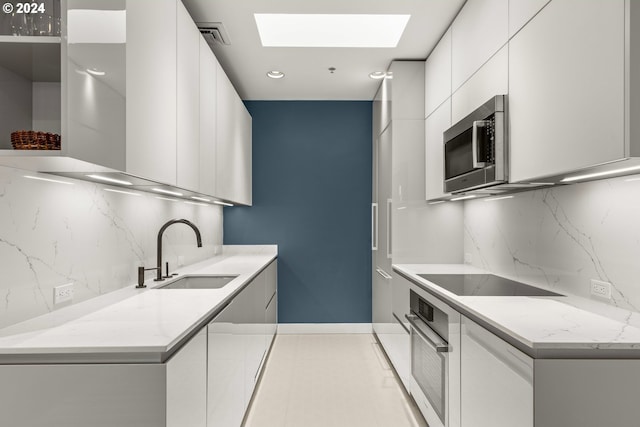 kitchen featuring sink, a skylight, backsplash, white cabinetry, and appliances with stainless steel finishes