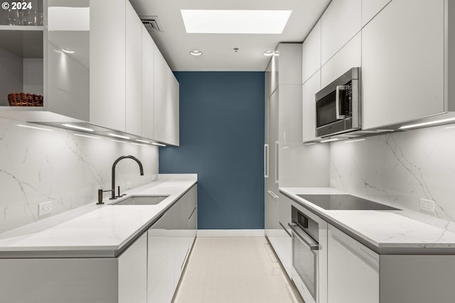 618 NW 12th Ave Unit 409, Portland, OR 97209 - kitchen featuring a sink, appliances with stainless steel finishes, modern cabinets, wall chimney range hood, and a skylight