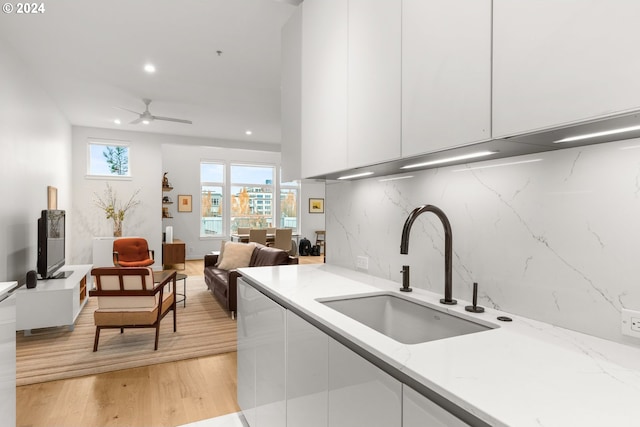 kitchen with white cabinetry, light wood-type flooring, light stone countertops, sink, and ceiling fan