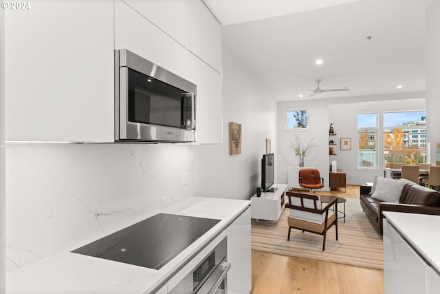 kitchen with light hardwood / wood-style floors, light stone counters, white cabinets, backsplash, and appliances with stainless steel finishes