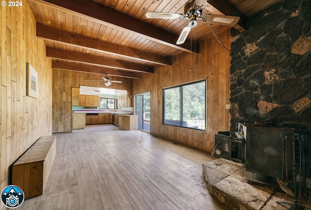 unfurnished living room with wood ceiling, light hardwood / wood-style floors, a wood stove, wood walls, and beam ceiling