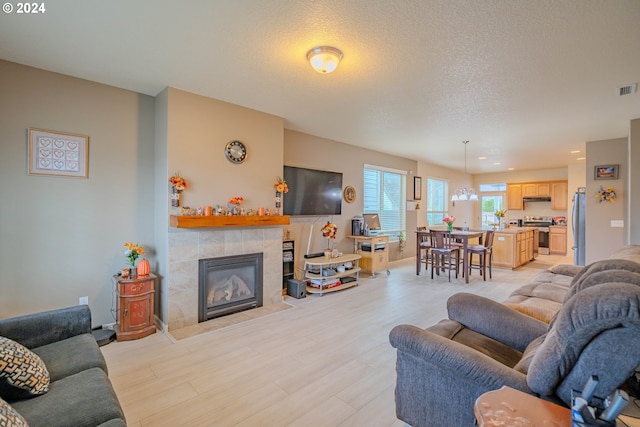 living room with an inviting chandelier, a textured ceiling, a fireplace, and light wood-type flooring