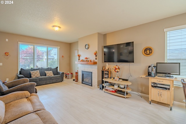 living room featuring a tiled fireplace, a textured ceiling, and light hardwood / wood-style floors