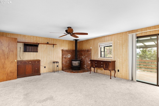 carpeted living room featuring a wood stove, ceiling fan, an AC wall unit, and wooden walls