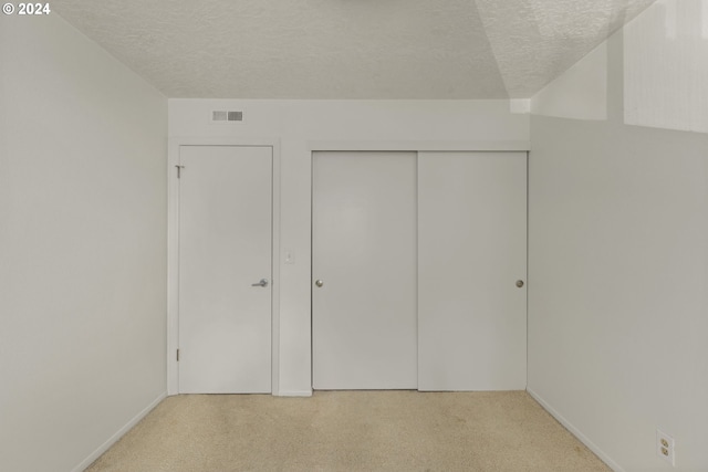 unfurnished bedroom featuring a closet, light colored carpet, and a textured ceiling