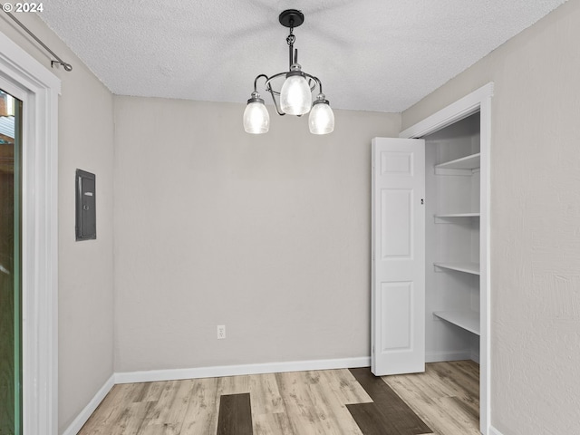 unfurnished dining area with light hardwood / wood-style floors, a textured ceiling, and an inviting chandelier