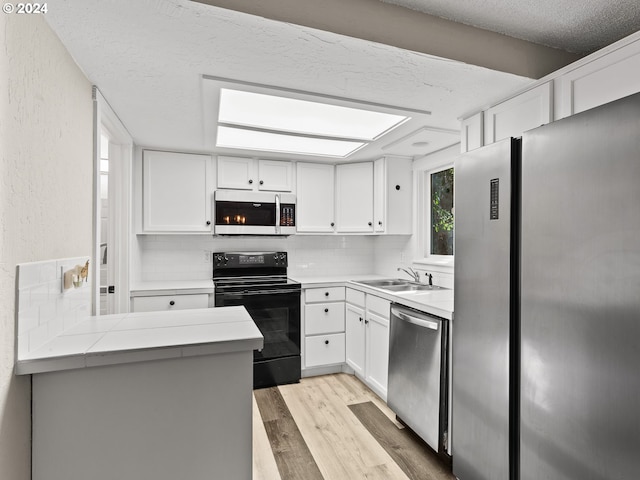 kitchen with kitchen peninsula, appliances with stainless steel finishes, light wood-type flooring, tasteful backsplash, and white cabinetry