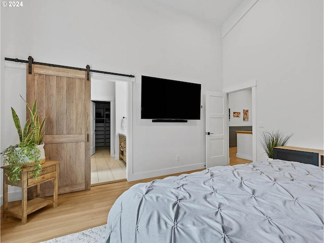 bedroom featuring a high ceiling, wood-type flooring, ensuite bathroom, and a barn door