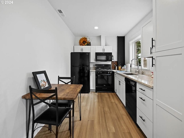 kitchen with a sink, visible vents, black appliances, and white cabinetry