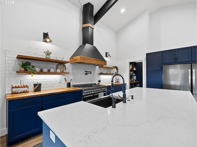 kitchen with blue cabinets, open shelves, a sink, backsplash, and wall chimney exhaust hood