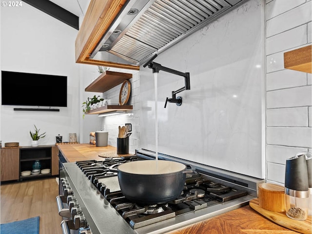 kitchen with premium range hood, hardwood / wood-style flooring, stainless steel gas range, and butcher block countertops