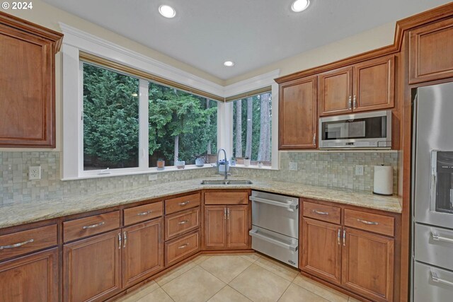 kitchen with appliances with stainless steel finishes, backsplash, light stone countertops, light tile patterned floors, and sink