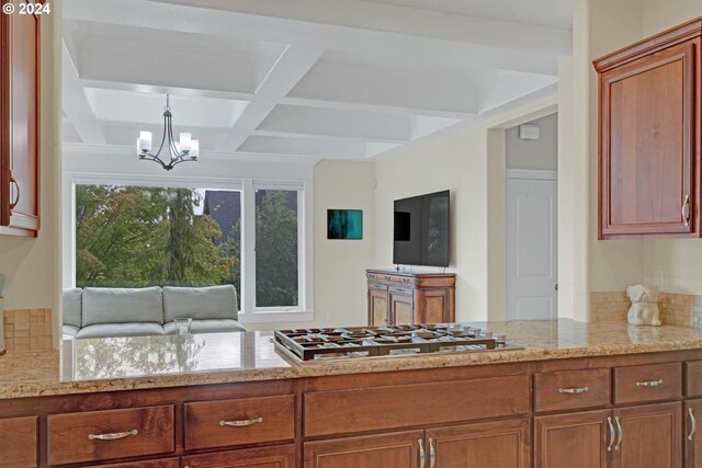 kitchen featuring pendant lighting, a chandelier, stainless steel gas cooktop, coffered ceiling, and light stone countertops