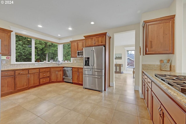 kitchen with tasteful backsplash, light stone countertops, light tile patterned floors, stainless steel appliances, and sink