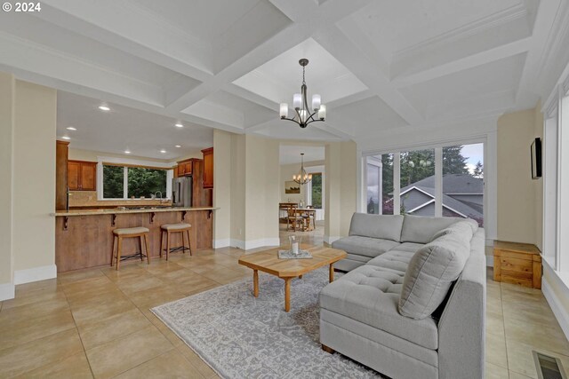 tiled living room with a notable chandelier, beam ceiling, coffered ceiling, and crown molding