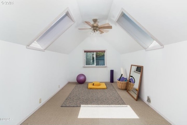 workout room with light carpet, ceiling fan, and vaulted ceiling with skylight