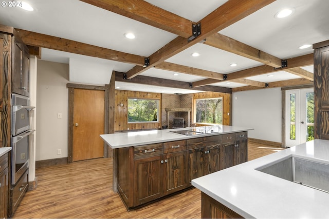 kitchen featuring an island with sink, beam ceiling, light hardwood / wood-style flooring, and black electric cooktop