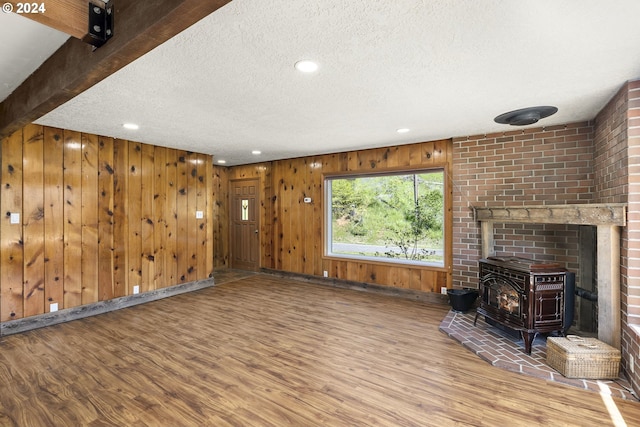 unfurnished living room featuring brick wall, wood-type flooring, a wood stove, and wood walls