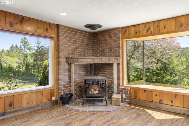 unfurnished living room featuring a healthy amount of sunlight, wood walls, a wood stove, and hardwood / wood-style floors