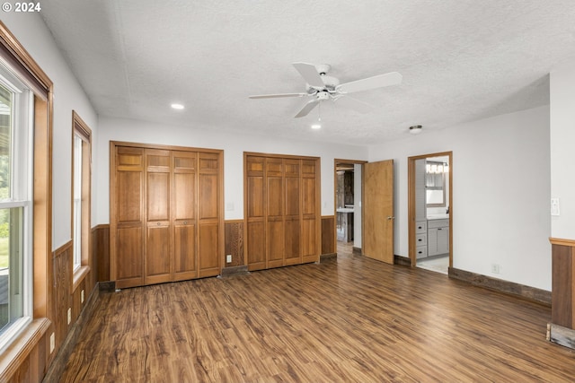 unfurnished bedroom with dark wood-type flooring, ensuite bathroom, two closets, and ceiling fan