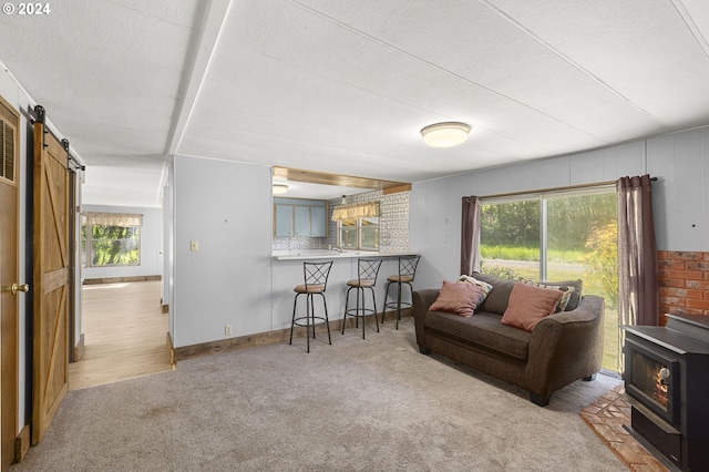 living room with a barn door, a healthy amount of sunlight, light carpet, and a wood stove