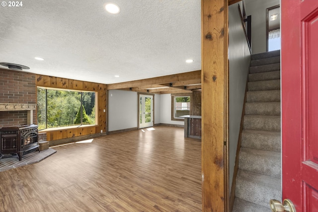 unfurnished living room featuring dark hardwood / wood-style flooring, a textured ceiling, a wood stove, brick wall, and wood walls