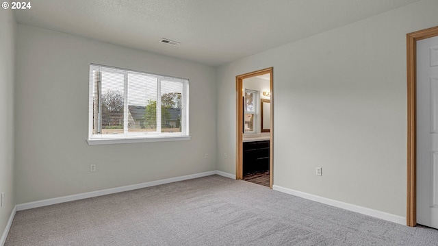 unfurnished bedroom with a textured ceiling, carpet floors, and ensuite bathroom