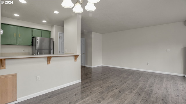 kitchen with stainless steel fridge, green cabinets, dark hardwood / wood-style flooring, a breakfast bar area, and kitchen peninsula