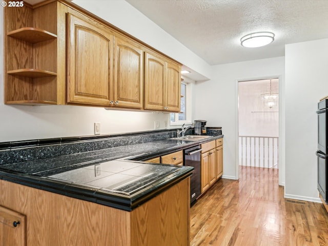 kitchen featuring light wood-style flooring, a sink, a textured ceiling, dishwasher, and baseboards