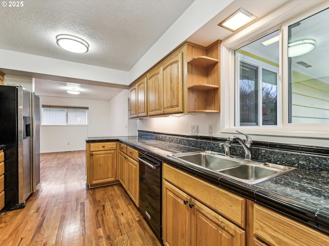 kitchen with black dishwasher, dark countertops, a sink, stainless steel fridge, and hardwood / wood-style floors