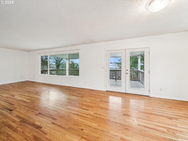 spare room featuring french doors, baseboards, a textured ceiling, and light wood finished floors