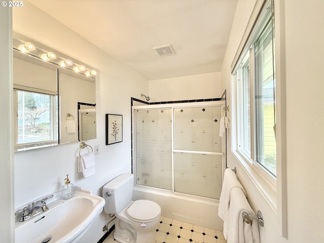 bathroom with toilet, bath / shower combo with glass door, a sink, and visible vents