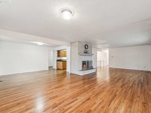 unfurnished living room featuring a fireplace, a textured ceiling, and light wood-type flooring