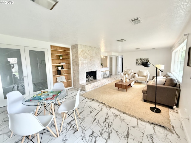 living room featuring built in shelves, marble finish floor, visible vents, and a tiled fireplace