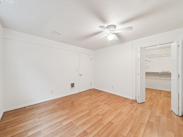 unfurnished bedroom featuring ceiling fan, visible vents, baseboards, light wood finished floors, and a walk in closet