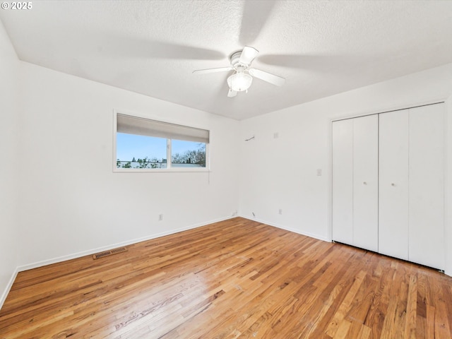 unfurnished bedroom featuring a textured ceiling, light wood-style flooring, visible vents, baseboards, and a closet