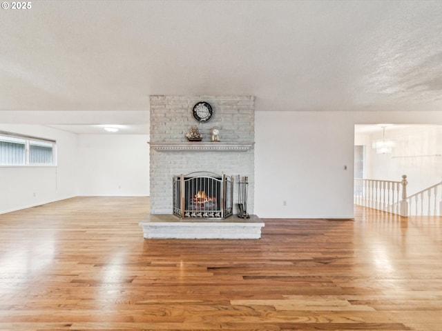 unfurnished living room featuring a textured ceiling, a brick fireplace, wood finished floors, and an inviting chandelier