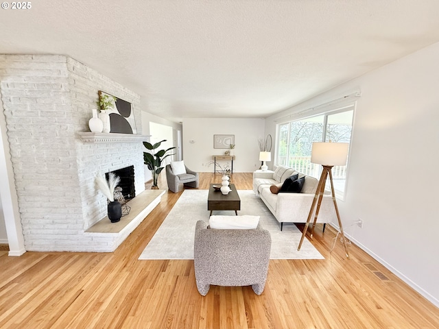 living area with baseboards, visible vents, a textured ceiling, light wood-type flooring, and a brick fireplace