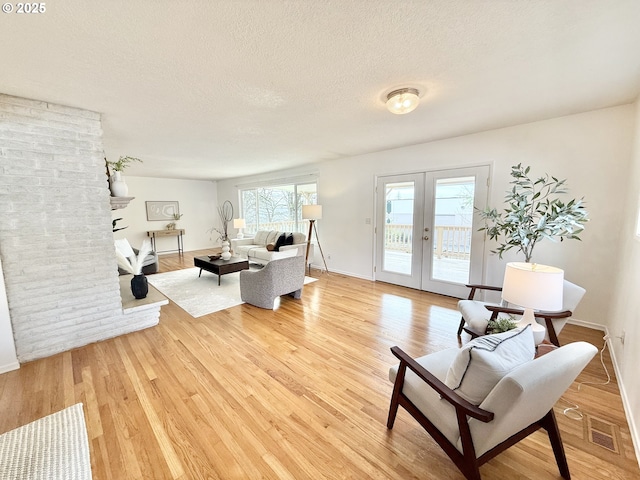 living area featuring light wood finished floors, baseboards, visible vents, a textured ceiling, and french doors