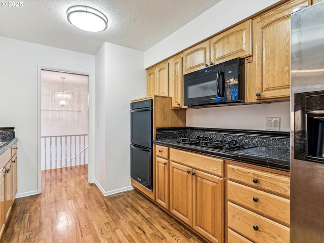 kitchen featuring dark countertops, light wood finished floors, black appliances, and a textured ceiling