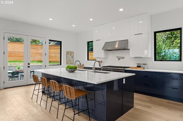 kitchen featuring light hardwood / wood-style floors, a kitchen island with sink, wall chimney exhaust hood, and sink