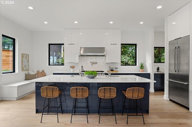 kitchen with a center island with sink, light hardwood / wood-style floors, range hood, and built in refrigerator