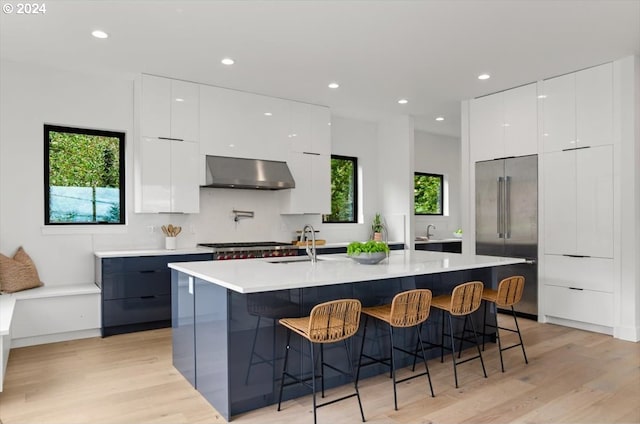 kitchen featuring appliances with stainless steel finishes, wall chimney exhaust hood, white cabinetry, and an island with sink