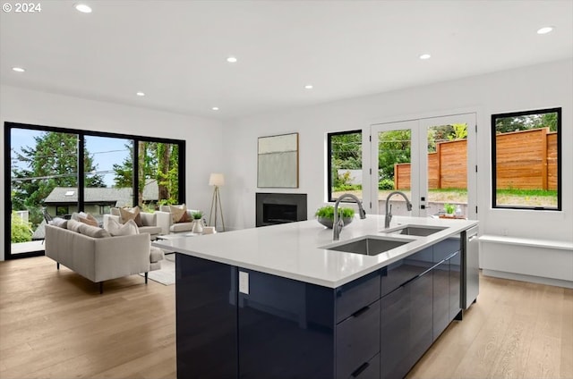 kitchen with a center island with sink, stainless steel dishwasher, sink, and light hardwood / wood-style flooring